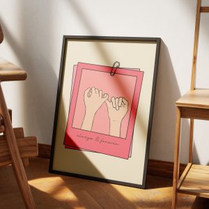 A framed poster with a minimalistic design featuring two hands making a pinky promise, set against a beige background with pink borders. The text "always & forever" is written at the bottom. The poster is leaning against a wooden easel, illuminated by soft natural light, with a macrame wall hanging visible in the background.