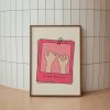 A framed poster with a minimalistic design featuring two hands making a pinky promise, set against a beige background with pink borders. The text "always & forever" is written at the bottom. The poster is leaning against a tiled wall with a light wood frame, placed on the floor.