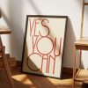 A beige framed poster with red text reading "YES YOU CAN" in a modern, minimalist font is leaning against a white wall. The poster rests on a wooden floor, with sunlight casting a shadow across it, adding depth and warmth to the scene.